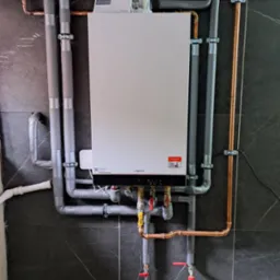 Kocioł grzewczy Viessmann z orurowaniem miedzianym i izolowanym, zamontowany na ścianie wyłożonej ciemnymi płytkami imitującymi marmur.