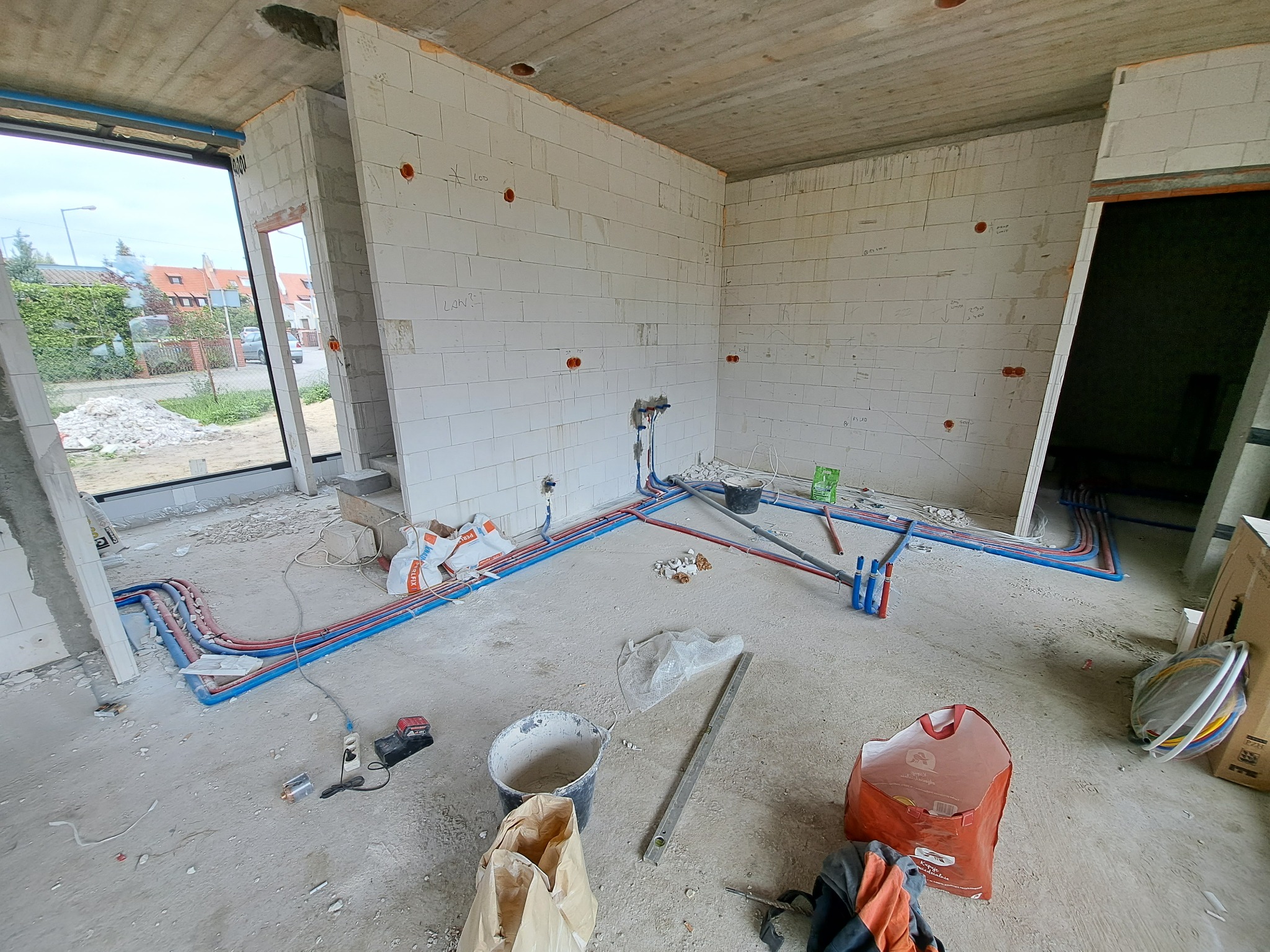 Surowy stan: Instalacja wodna i ogrzewania podłogowego w trakcie montażu w nowym domu, widoczne rury w kolorze niebieskim i czerwonym, ściany z betonu komórkowego z zaznaczonymi punktami...