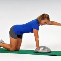 Kobieta w Tarnowskich Górach wykonuje ćwiczenie stabilizacyjne na macie z użyciem poduszki sensomotorycznej, unosząc prawą rękę i lewą nogę.