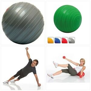 Zestaw do ćwiczeń: szara i zielona piłka gimnastyczna, małe hantle i dwie osoby wykonujące ćwiczenia, mężczyzna w pozycji bocznej deski z hantlą w górze, kobieta leżąca na piłce z hantlami w rękach.