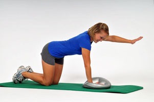 Kobieta w Tarnowskich Górach wykonuje ćwiczenie stabilizacyjne na macie z użyciem poduszki sensomotorycznej, unosząc prawą rękę i lewą nogę.