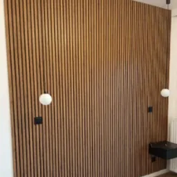 Ściana wykończona panelami drewnianymi z czarnymi szczelinami, oświetlona kulistymi lampami wiszącymi i z zamontowaną czarną szafką nocną.