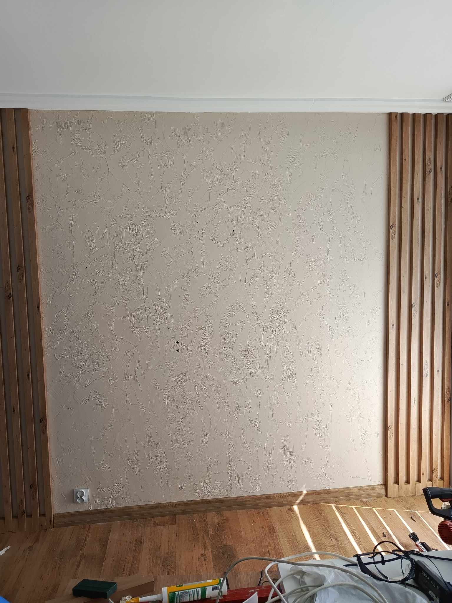 Ściana z dekoracyjnymi, drewnianymi lamelami po bokach w mieszkaniu w Warszawie, widoczne narzędzia i akcesoria montażowe na podłodze.