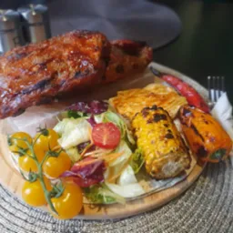 Grillowane żeberka z kukurydzą, serem halloumi i sałatką na drewnianej desce, podane na kamiennej płycie.