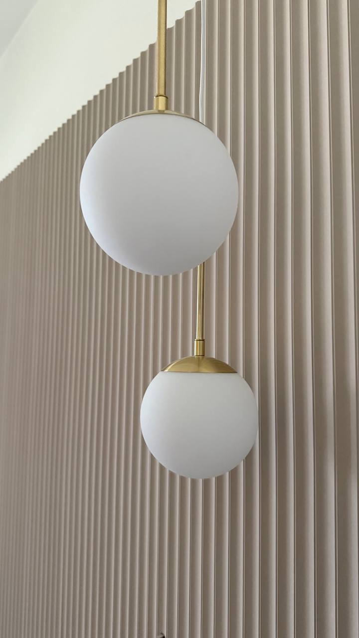 Nowoczesna ściana z lamelami w beżowym odcieniu i minimalistyczna lampa kulista z elementami w kolorze złota, tworząca elegancki detal wnętrza.