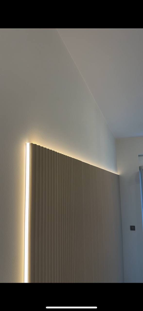 Beżowa ściana z dekoracyjnymi lamelami i subtelnym oświetleniem LED, tworzącymi nowoczesny akcent w wykończeniu wnętrza.