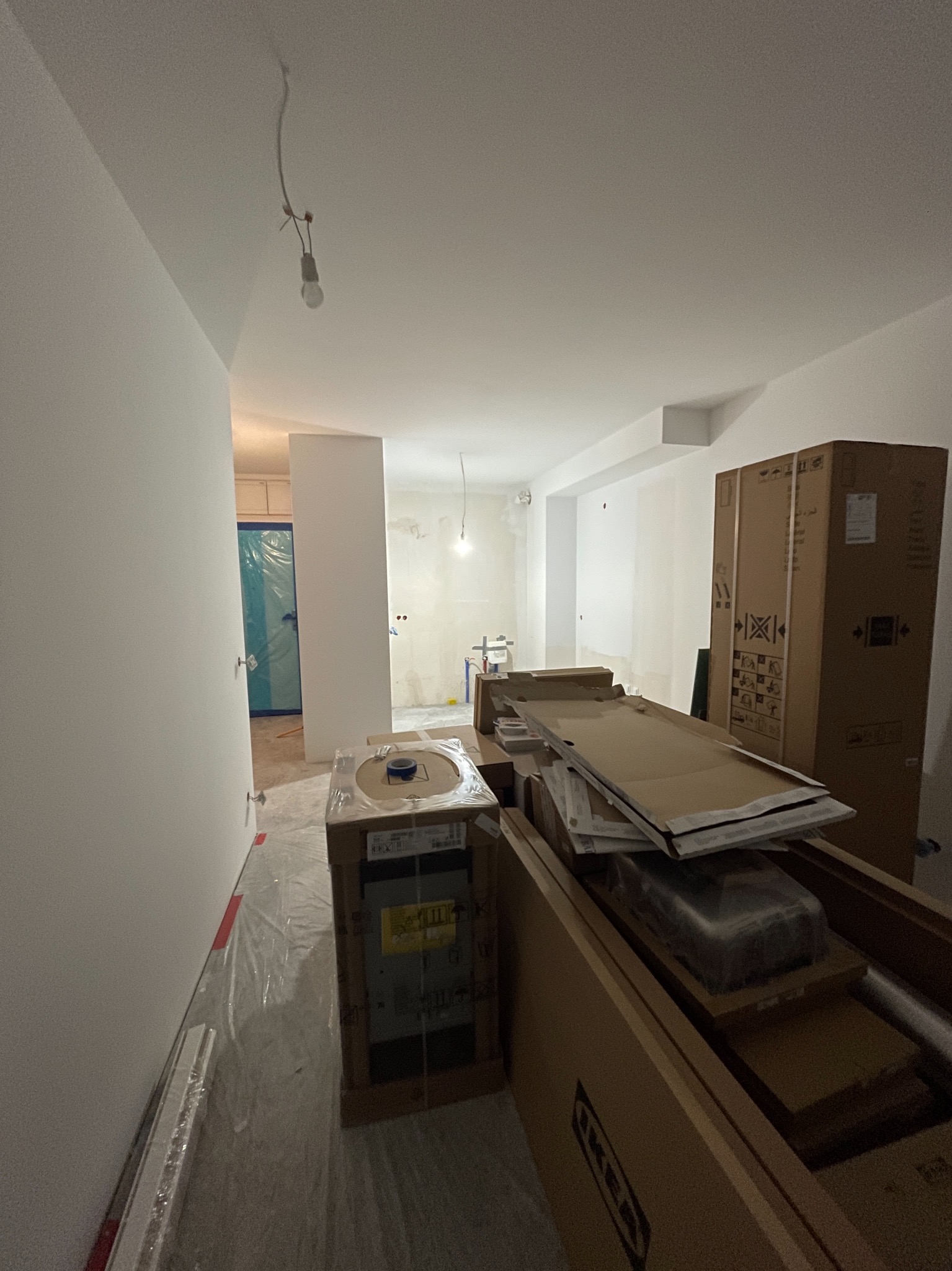 Wnętrze w trakcie remontu: białe ściany, podłoga zabezpieczona folią, kartony z wyposażeniem IKEA, widoczne instalacje i surowy stan pomieszczenia.