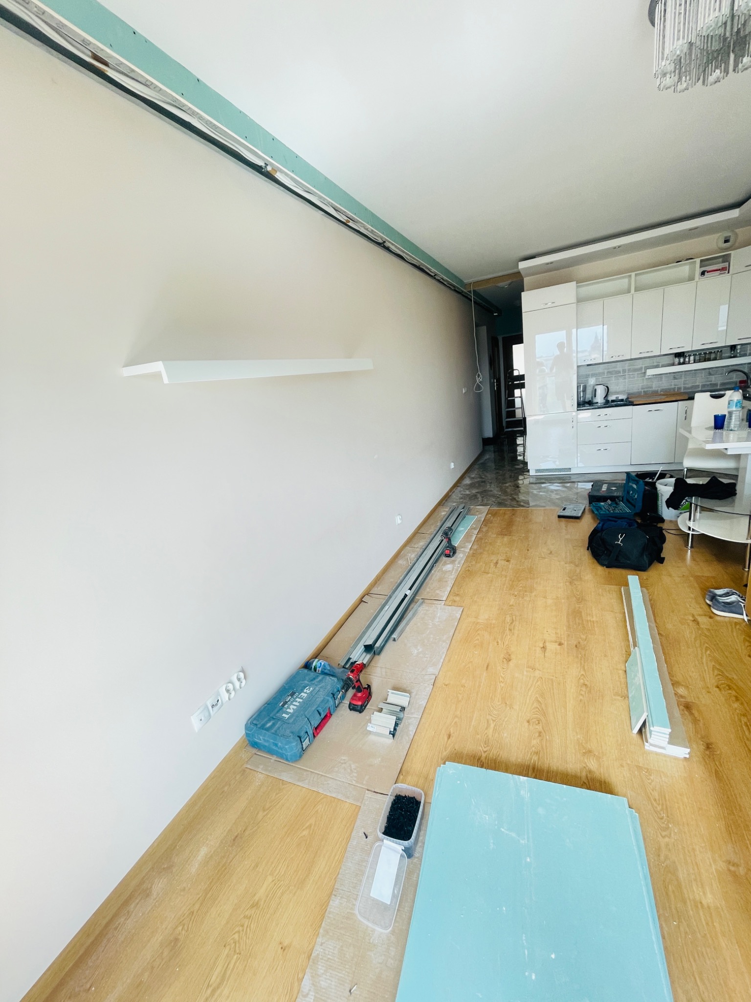 Wnętrze mieszkania w trakcie prac remontowych, widoczne narzędzia, płyty oraz listwy przyścienne, zamontowany profil pod zabudowę karton-gips na ścianie, w tle kuchnia z białymi szafkami.