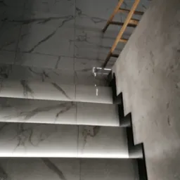 Nowoczesne schody z podświetleniem LED, wykończone płytkami imitującymi marmur, z widoczną drewnianą drabiną w tle i surową, szpachlowaną ścianą.