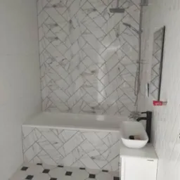 Wykończona łazienka z biało-szarą marmurkową glazurą ułożoną w jodełkę na ścianie nad wanną, białą umywalką nablatową z czarną baterią i podłogą w biało-czarne płytki o geometrycznym wzorze.