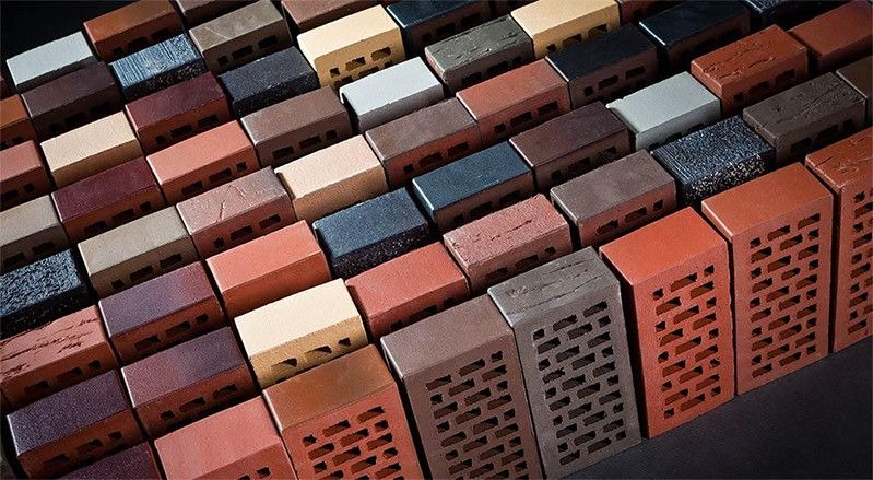Różnorodność cegieł klinkierowych w odcieniach czerwieni, brązu, beżu i szarości, ułożonych pod kątem, prezentujących faktury i wzory, niektóre z perforacją.