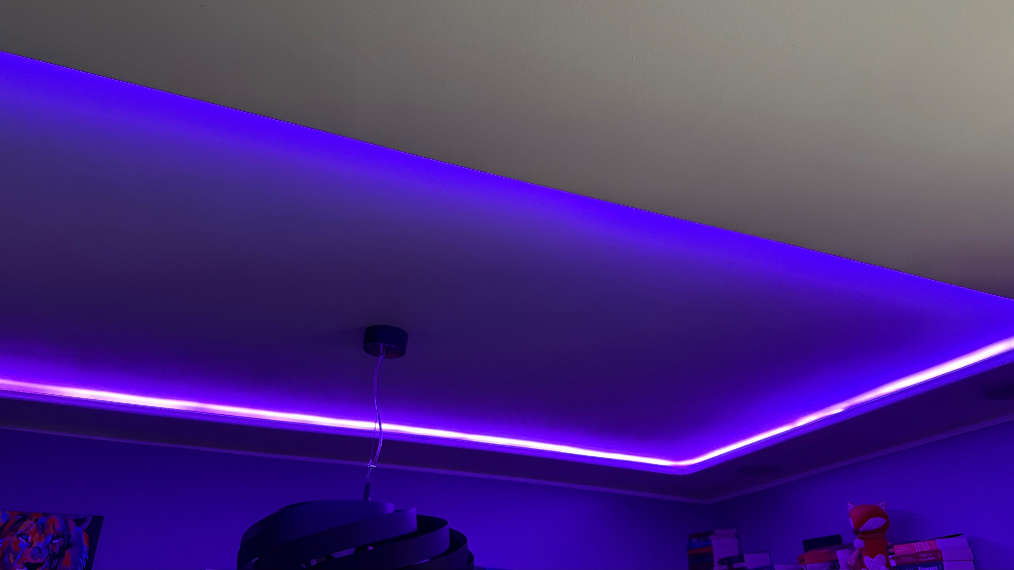 Podwieszany sufit z oświetleniem LED w odcieniach fioletu, widok z dołu, lampa wisząca w tle, nowoczesny design.