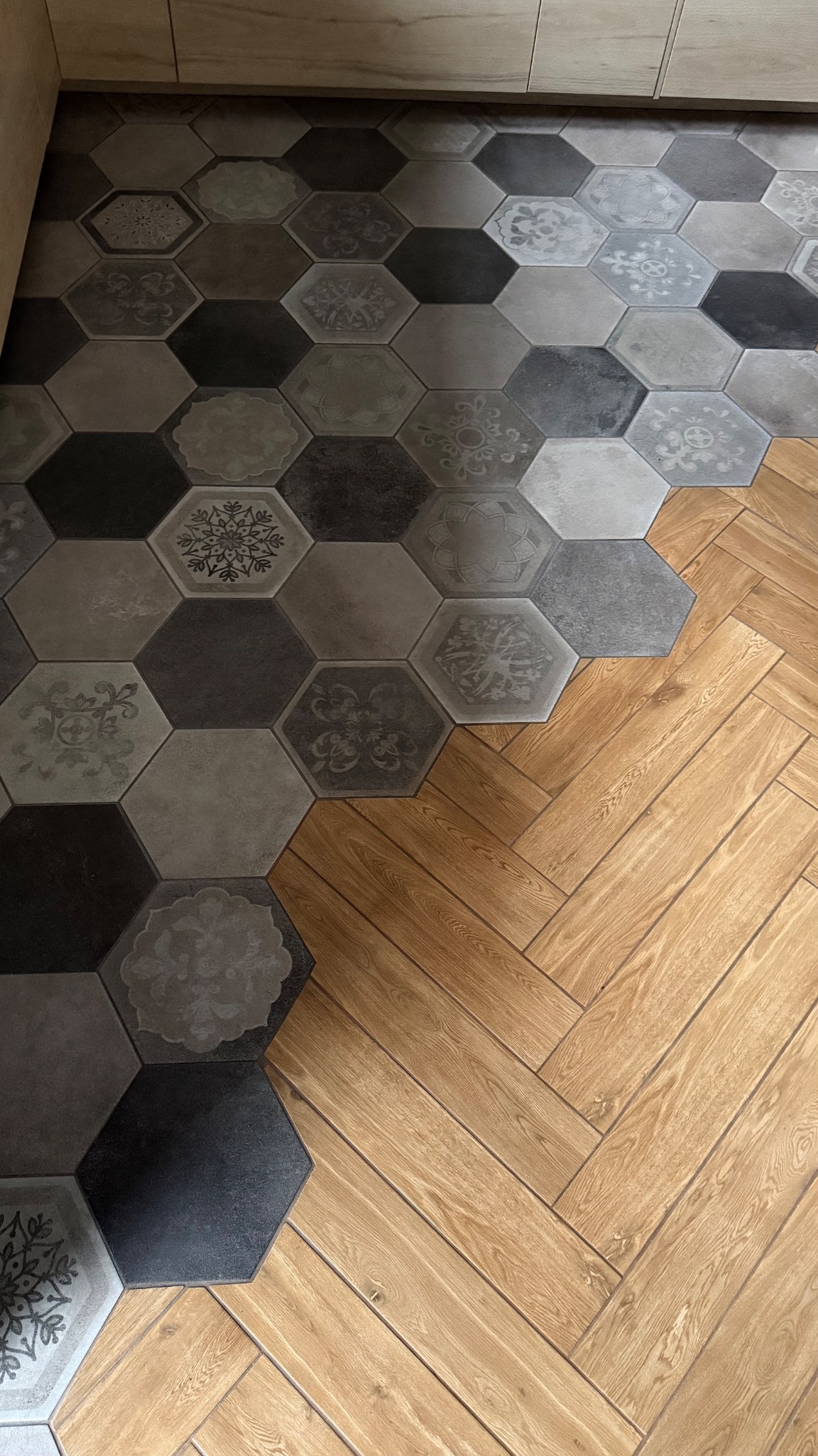 Kontrastowe wykończenie podłogi: heksagonalne płytki w odcieniach szarości z dekorami zestawione z drewnopodobnymi panelami ułożonymi w jodełkę.