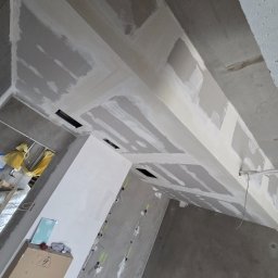 FIRMA REMONTOWO-WYKOŃCZENIOWA BORKOWSKI ŁUKASZ - Sufit podwieszany z płyt gipsowo-kartonowych w trakcie szpachlowania, widoczne otwory wentylacyjne i instalacje elektryczne na ścianach. Surowy stan wykończenia.