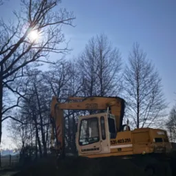 Żółta koparka Liebherr 316 na tle zimowego krajobrazu oświetlonego księżycem, widoczna z boku, z numerem telefonu na kabinie.