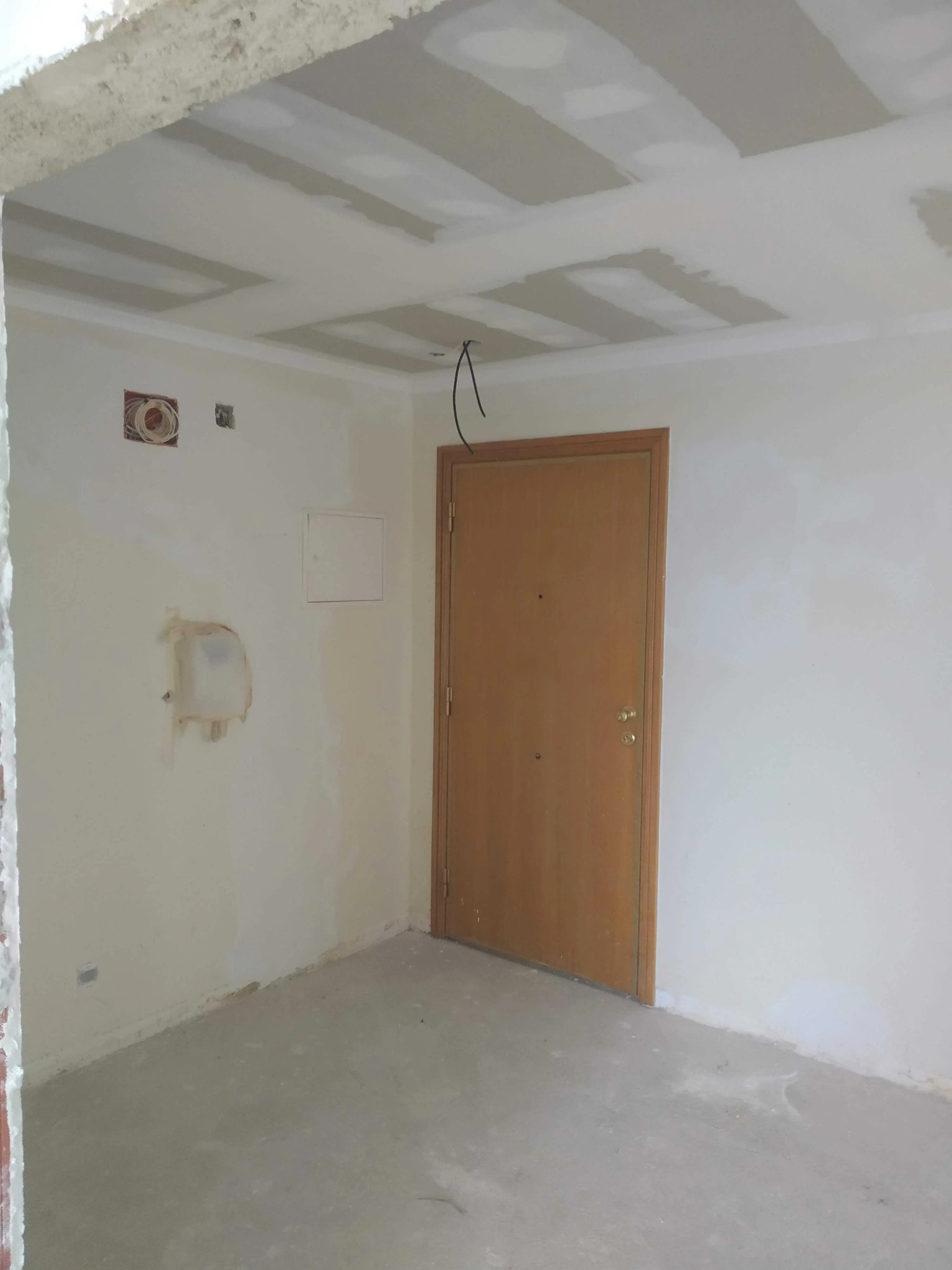 Pokój w trakcie prac wykończeniowych: surowy sufit z widocznymi płytami gipsowymi, ściany częściowo przygotowane do malowania z widocznymi puszkami elektrycznymi i śladami po instalacjach...