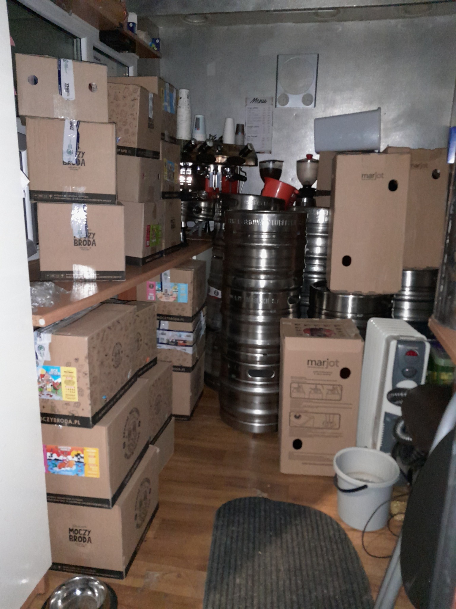 Wnętrze busa wypełnione kartonami z napisem 'Można Broda', beczkami, ekspresem do kawy i innymi przedmiotami, przygotowane do transportu.