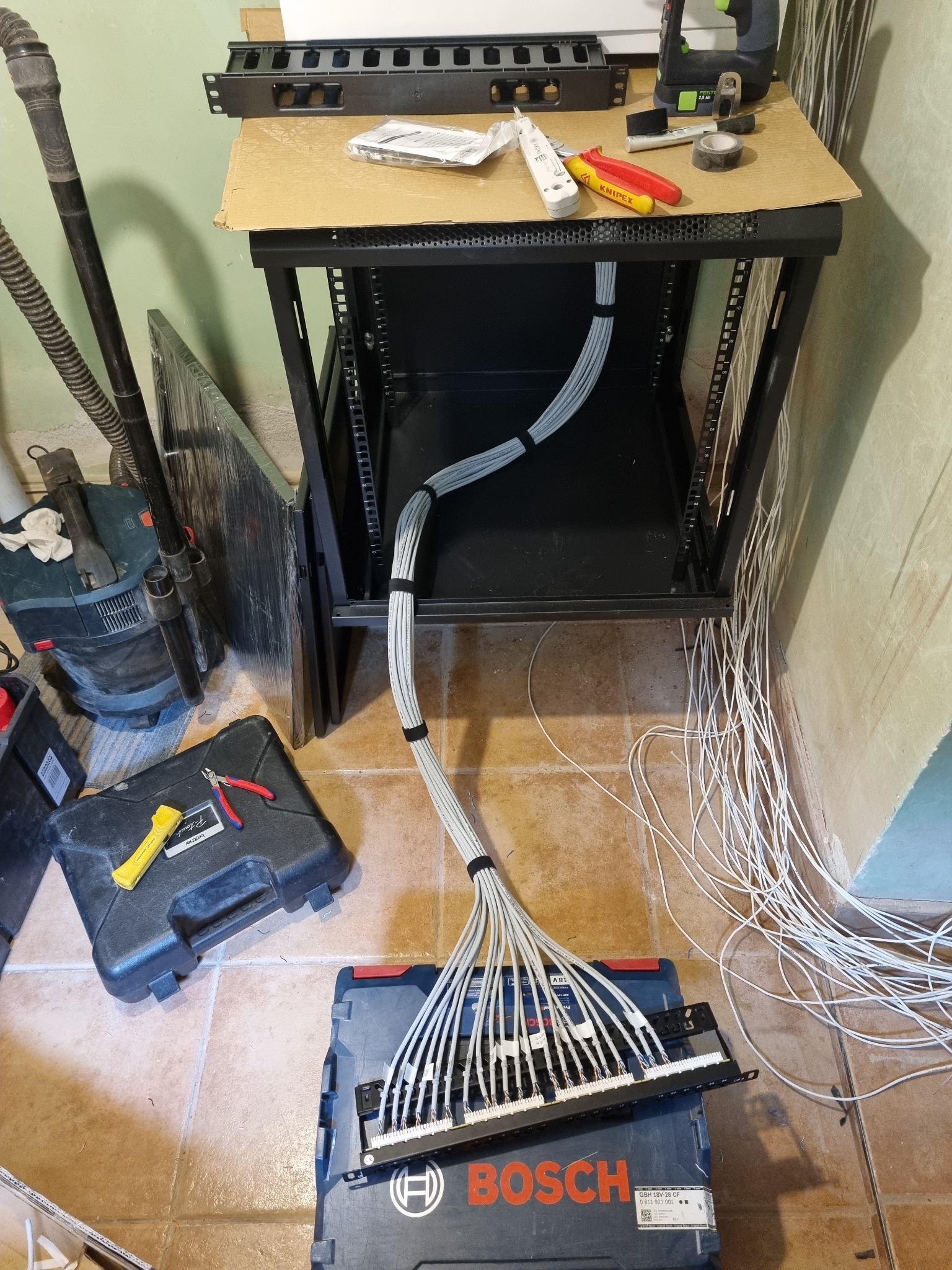 Montaż okablowania strukturalnego w szafie rack. Widoczne narzędzia, patch panel i uporządkowane kable. Prace instalacyjne w toku, z dbałością o porządek.