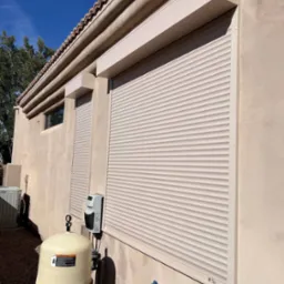 Zamknięte rolety zewnętrzne w kolorze beżowym na elewacji domu z widoczną instalacją basenową i błękitnym niebem w tle.