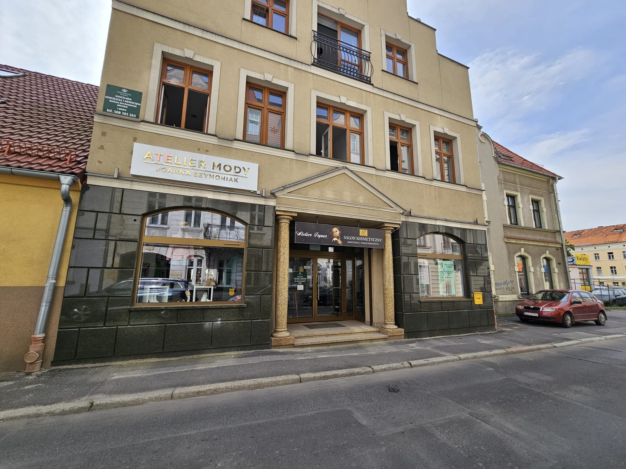 Fasada budynku z salonem kosmetycznym i atelier fryzur na parterze, z szyldem adwokackim na ścianie obok.