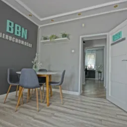 Wnętrze biura agencji nieruchomości w Białymstoku z okrągłym stołem, krzesłami i logo firmy na ścianie i drzwiach.