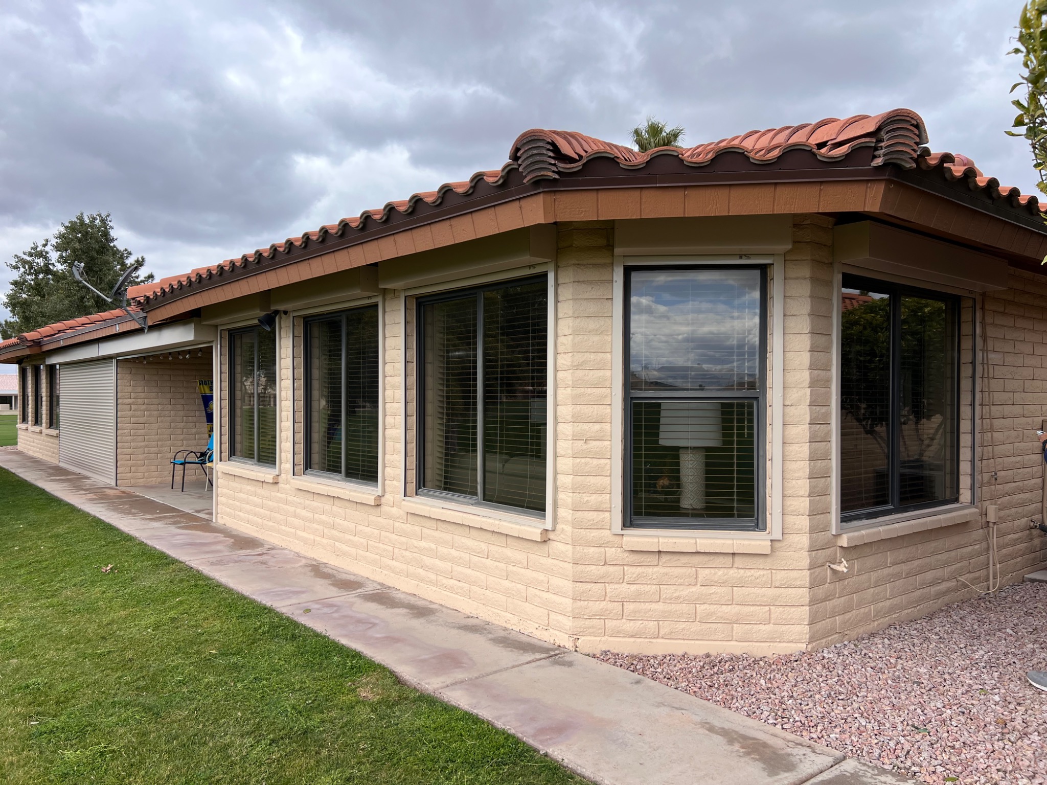 Dom z beżowej cegły z oknami osłoniętymi roletami zewnętrznymi, widok z zewnątrz na trawnik i chodnik.