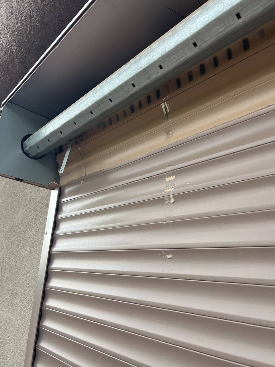Częściowo zwinięta brązowa roleta zewnętrzna z widocznymi śladami użytkowania i zabrudzeniami na listwach.