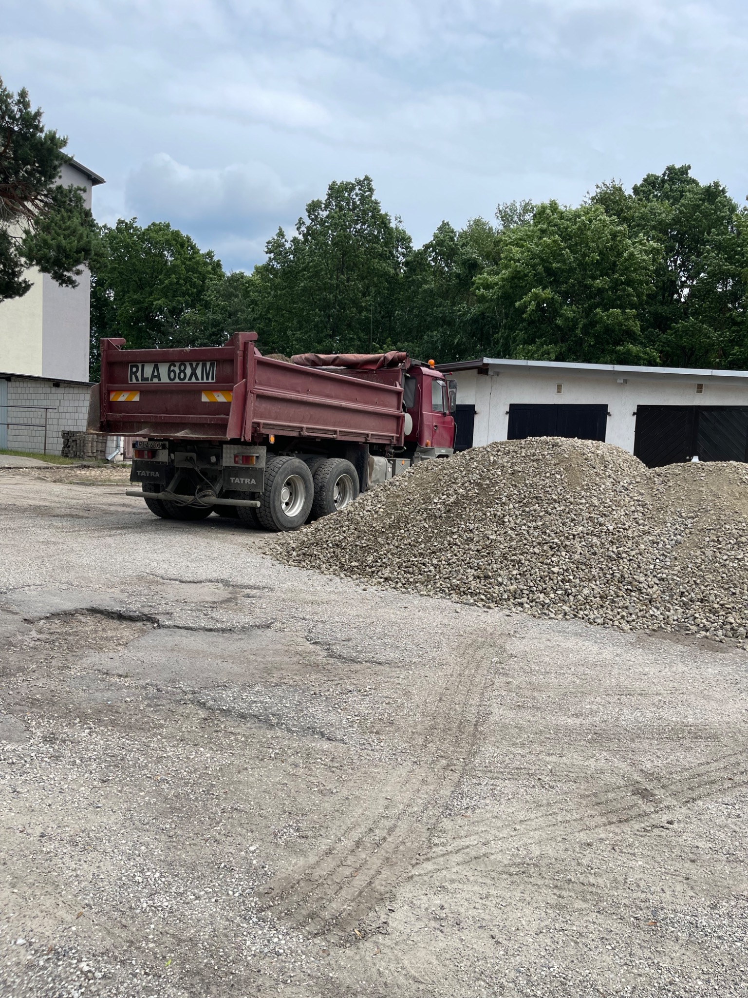 Czerwona wywrotka Tatra z numerem rejestracyjnym RLA 68XM stoi obok sporej pryzmy szarego kruszywa na placu, w tle budynek gospodarczy i drzewa.