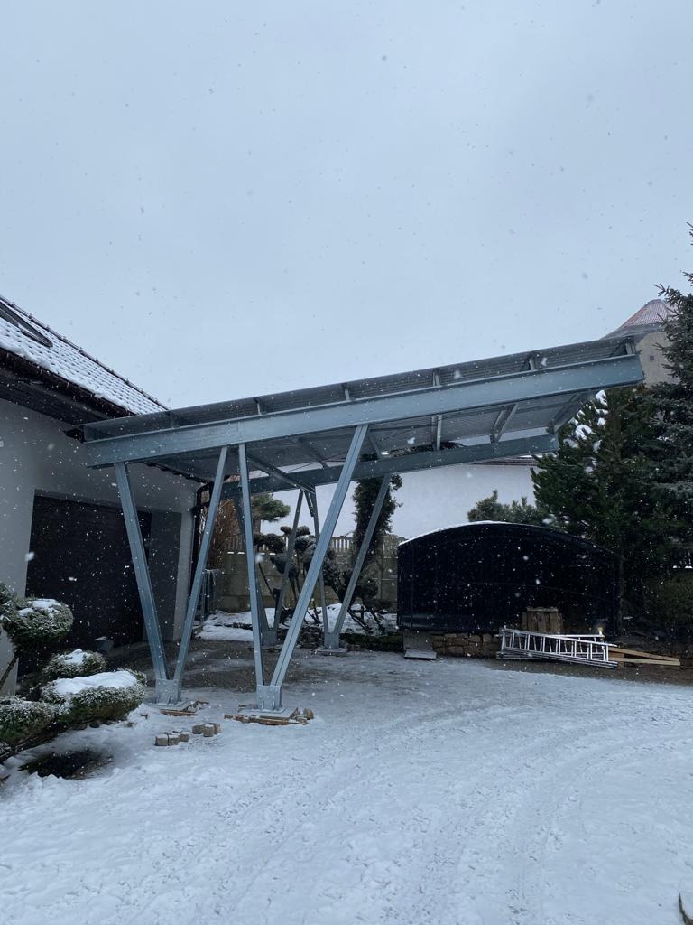 Metalowa konstrukcja wsporcza pod panele słoneczne w trakcie montażu, widoczny śnieg i rozłożone kostki brukowe.