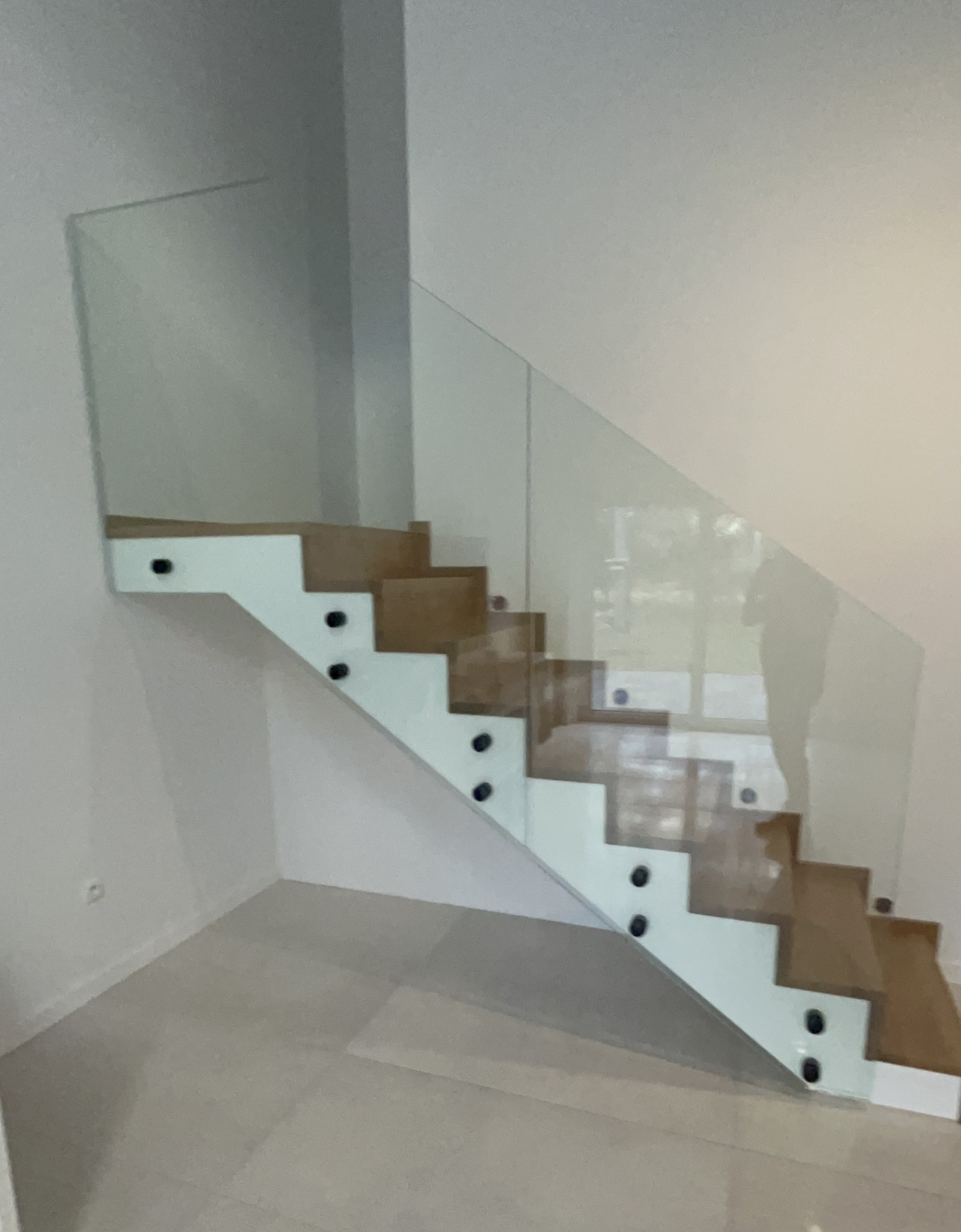 Szklana balustrada schodowa z drewnianymi stopniami, mocowana do boku schodów za pomocą rotul w kolorze czarnym.