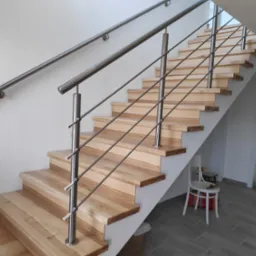 Schody drewniane z metalową balustradą, widok od dołu, z elementami wykończeniowymi w tle.