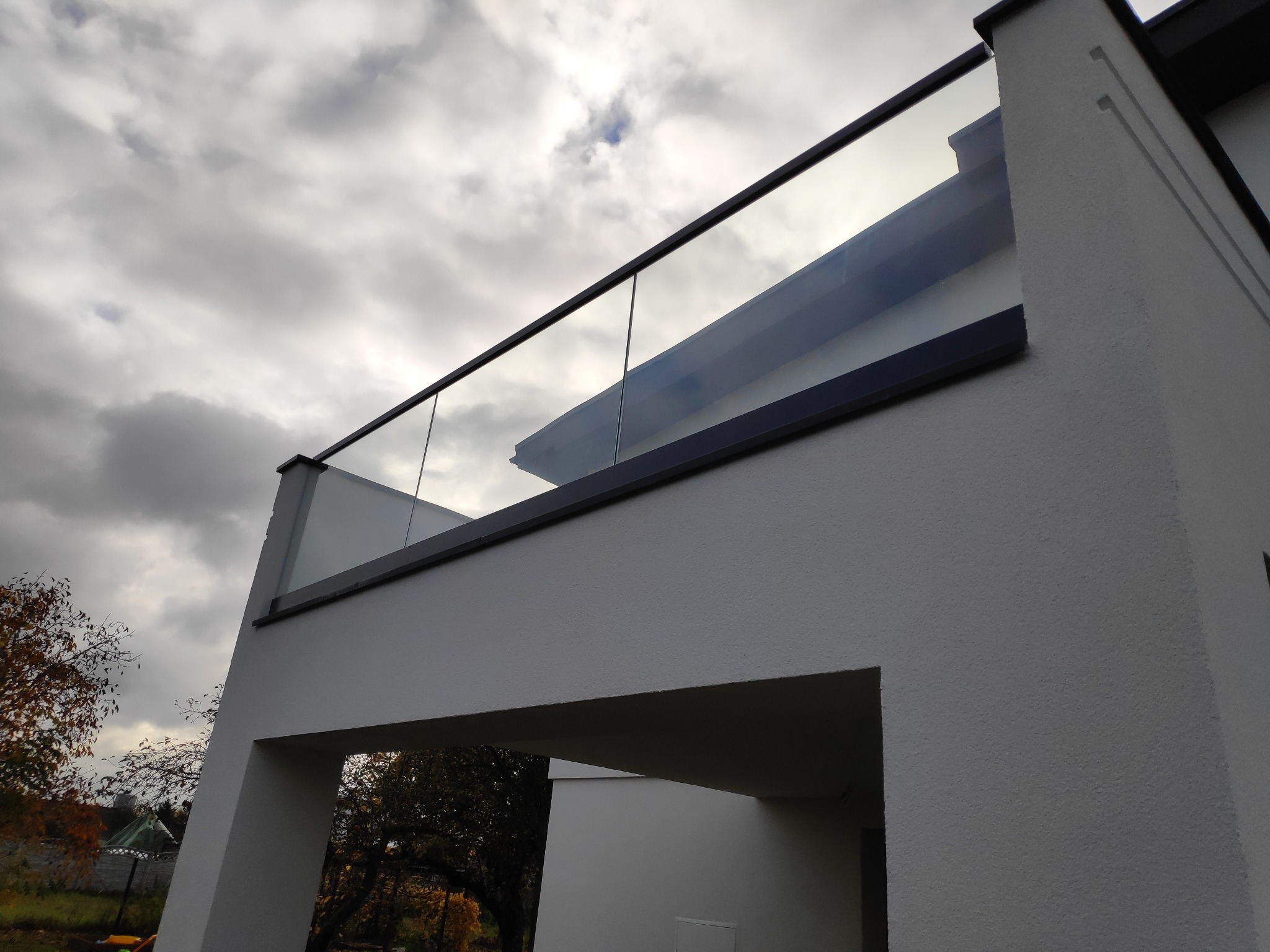 Nowoczesna szklana barierka balkonowa z czarną ramą na tle pochmurnego nieba, widok z dołu, minimalistyczna architektura.