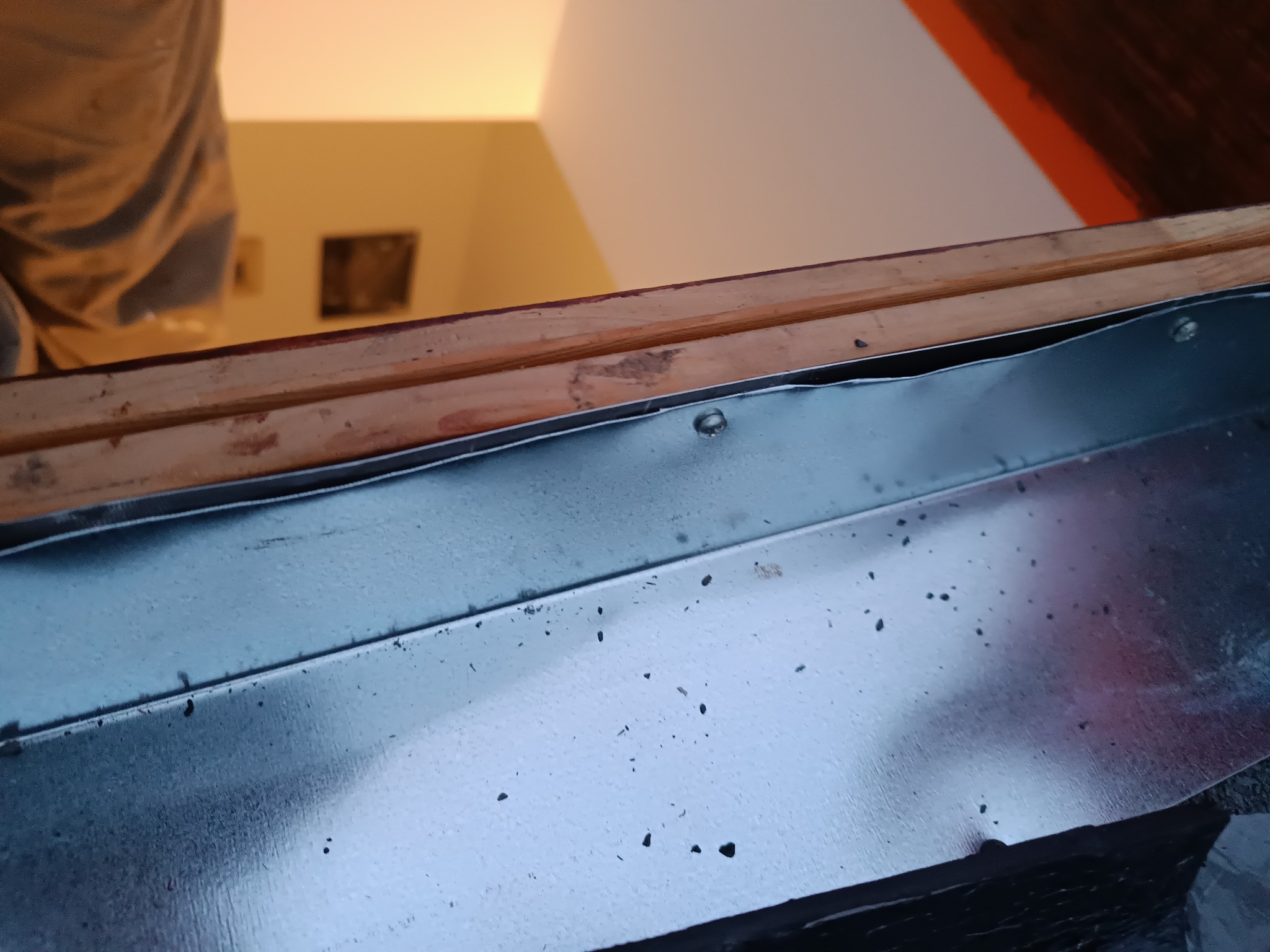 Metalowy okapnik okna dachowego przymocowany do drewnianej ramy, widoczne nity mocujące.