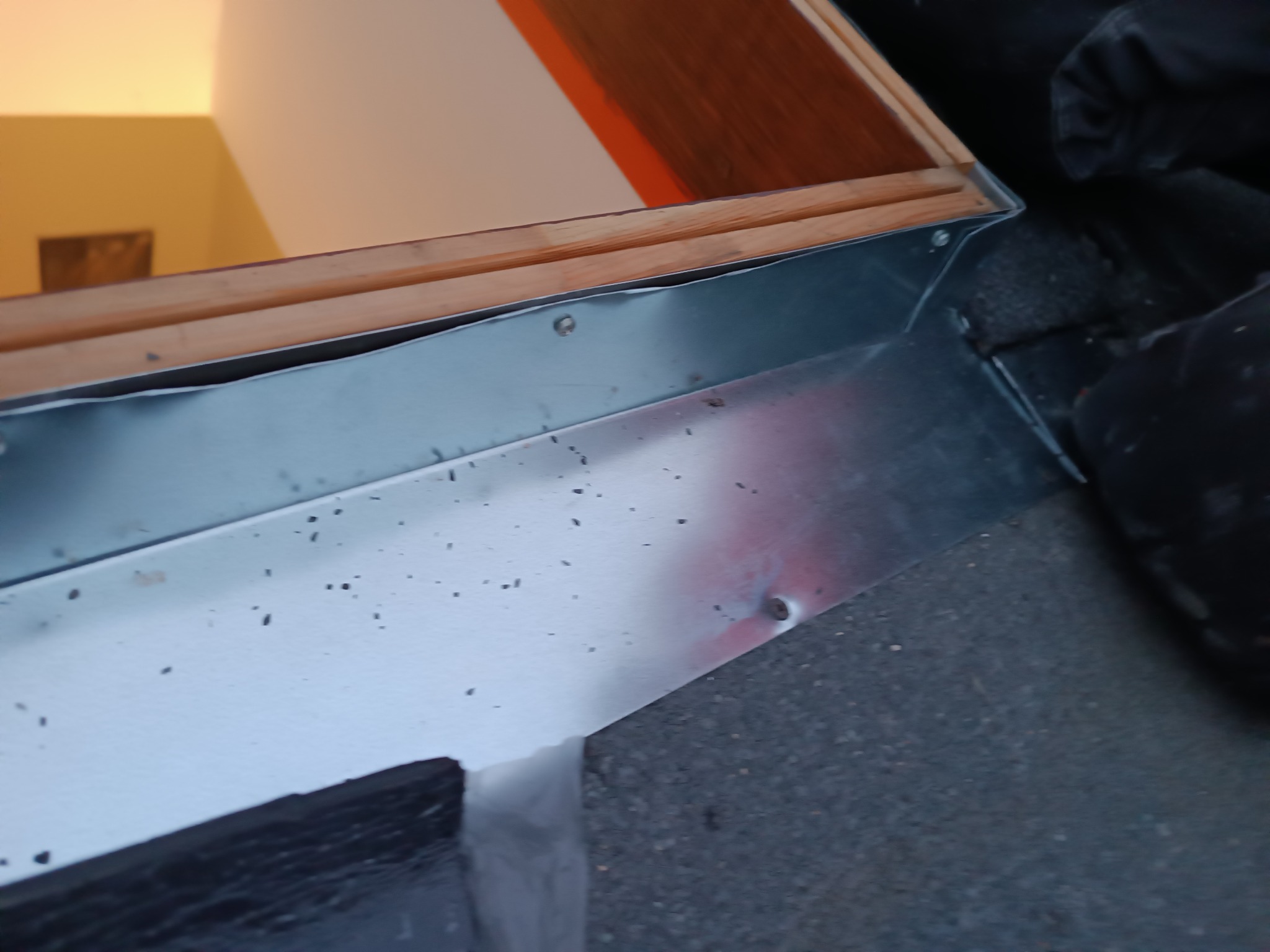 Metalowa obróbka blacharska okna dachowego z widocznymi nitami i śladami po lutowaniu, fragment dachu z papy w tle.