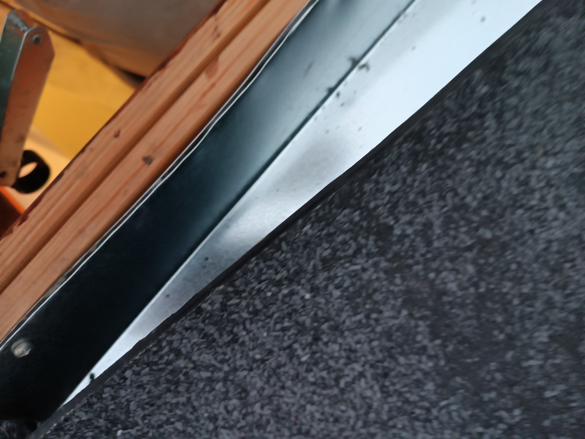 Fragment dachu z papą, drewnianą konstrukcją i metalowym obrzeżem, widoczne łączenie materiałów pod kątem.