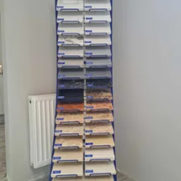Ekspozytor z próbkami parapetów z konglomeratu w różnych kolorach i wzorach, producent Polmar, widoczny grzejnik.
