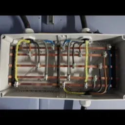 Rozdzielnica elektryczna z ułożonymi przewodami o różnych kolorach, podłączonymi do listew zaciskowych, widoczne kable wchodzące do puszki od góry i dołu.