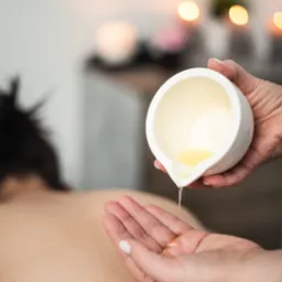 Terapeuta wlewa ciepły olejek z białej miseczki na dłoń pacjenta przygotowując się do zabiegu.