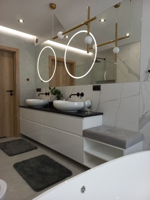 Nowoczesna łazienka z białymi szafkami pod umywalkę z czarnym blatem, okrągłymi umywalkami nablatowymi, dużym lustrem z podświetleniem LED w kształcie okręgów i designerskimi lampami wiszącymi...