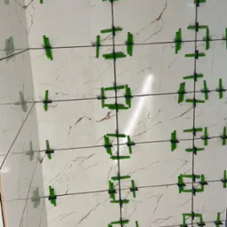 Ściana wyłożona białymi płytkami imitującymi marmur, z użyciem zielonych krzyżyków dystansowych, widoczne odbicie w narożniku.