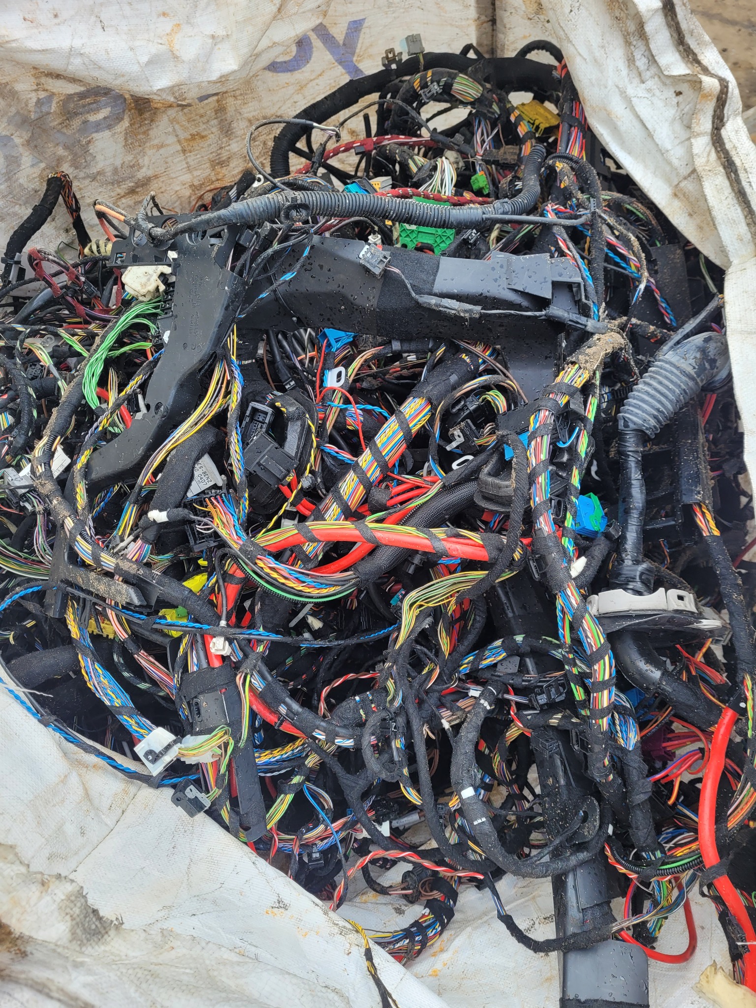 Stary, zdemontowany pęk przewodów samochodowych w worku z tworzywa sztucznego, widoczne różnokolorowe kable i wtyczki.