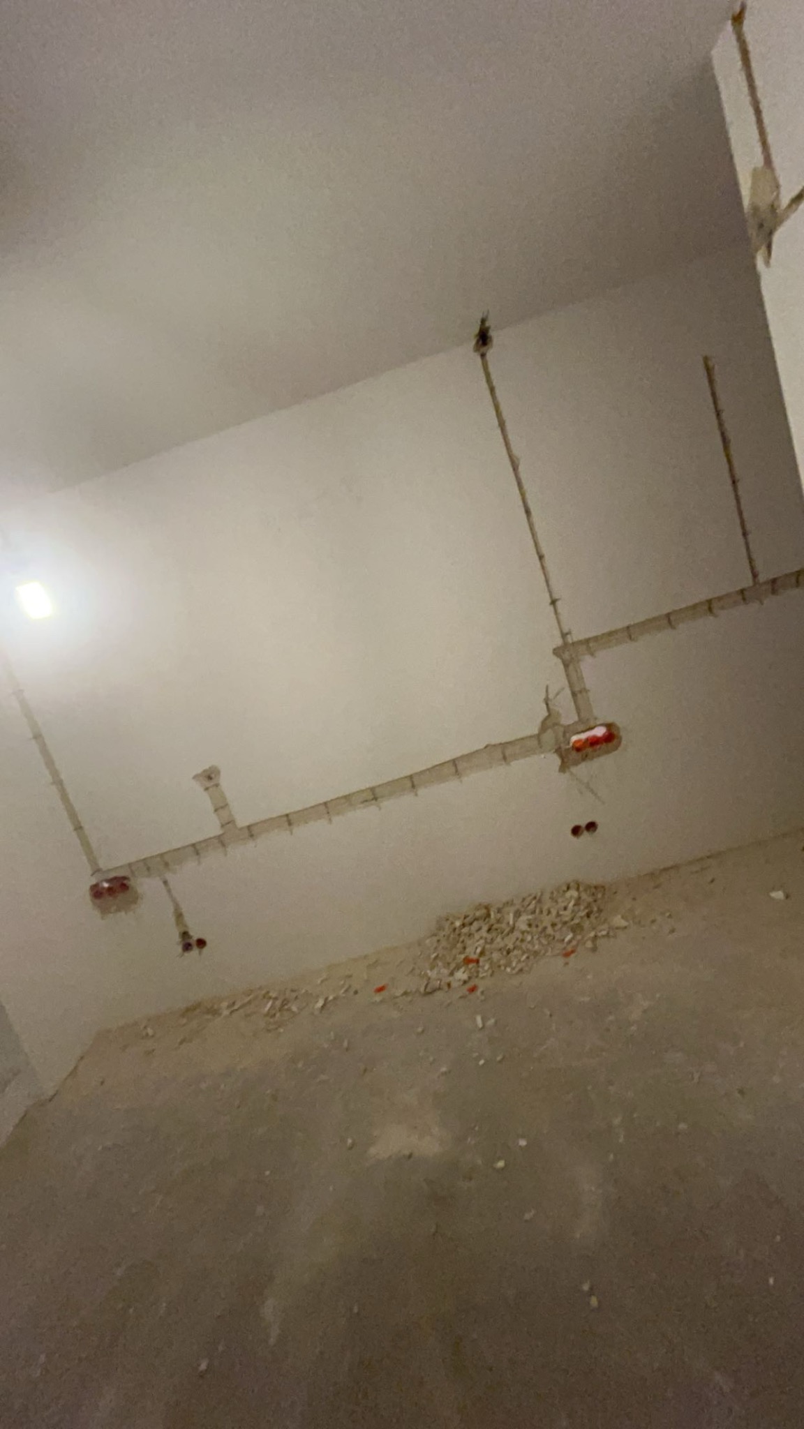 Wnętrze w trakcie remontu: widoczne poprowadzone kable elektryczne w rurkach na suficie i ścianach, gruz na podłodze, surowy stan wykończenia.