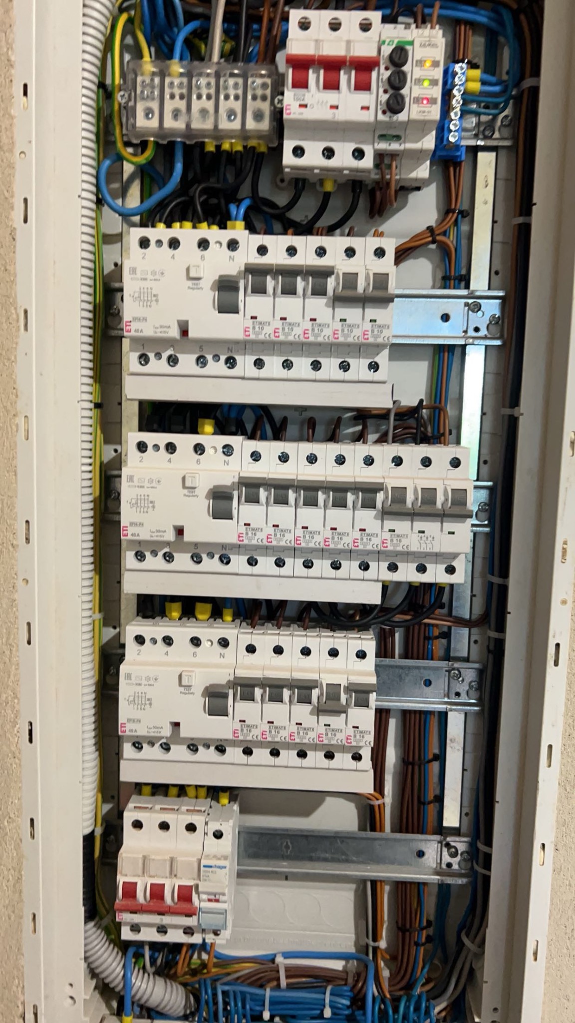 Rozdzielnica elektryczna z zainstalowanymi bezpiecznikami i okablowaniem wewnątrz białej obudowy, widoczne różne kolory przewodów i elementy mocujące.