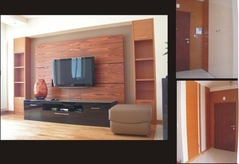 Nowoczesny salon z brązowymi meblami na wymiar, w tym szafki, półki i szafka RTV pod telewizorem na tle ściany z okładziną imitującą drewno. Dodatkowo widoczne fragmenty aranżacji przedpokoju...