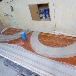 Pracownia Sgraffito - Przygotowanie elementów sztukaterii z gipsu na drewnianym stole w warsztacie, widoczne formy półkoliste i listwy, narzędzia i materiały budowlane w tle.