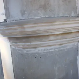 Fragment kolumny z dekoracyjnym gzymsem w trakcie prac renowacyjnych, widoczne ślady szpachlowania i niedoskonałości powierzchni.