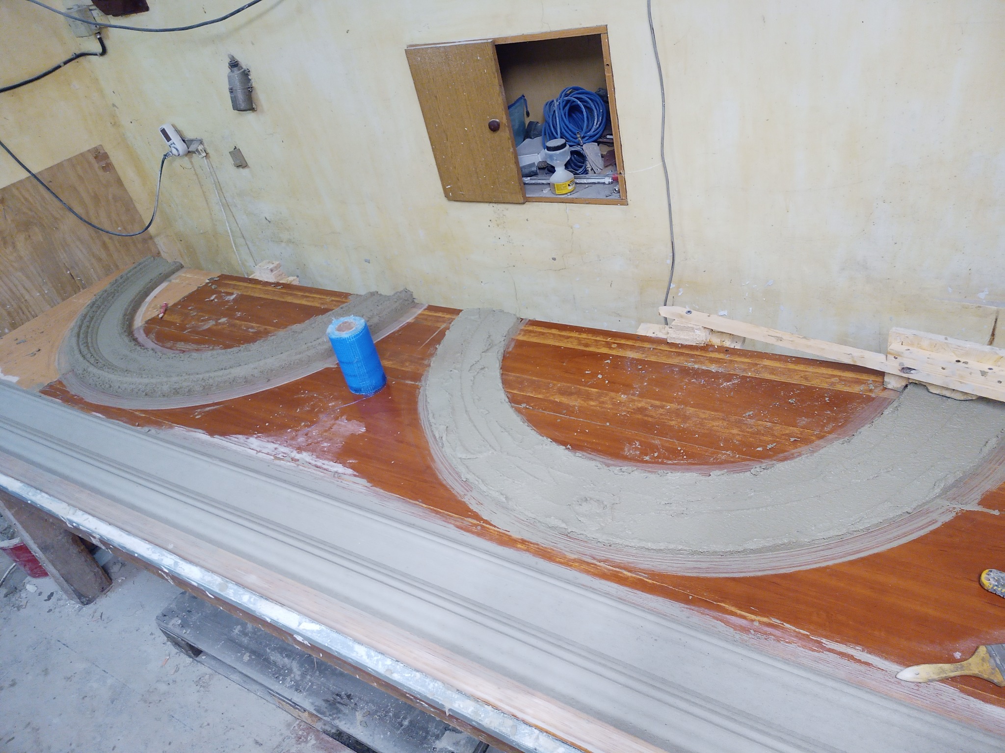 Przygotowanie elementów sztukaterii z gipsu na drewnianym stole w warsztacie, widoczne formy półkoliste i listwy, narzędzia i materiały budowlane w tle.