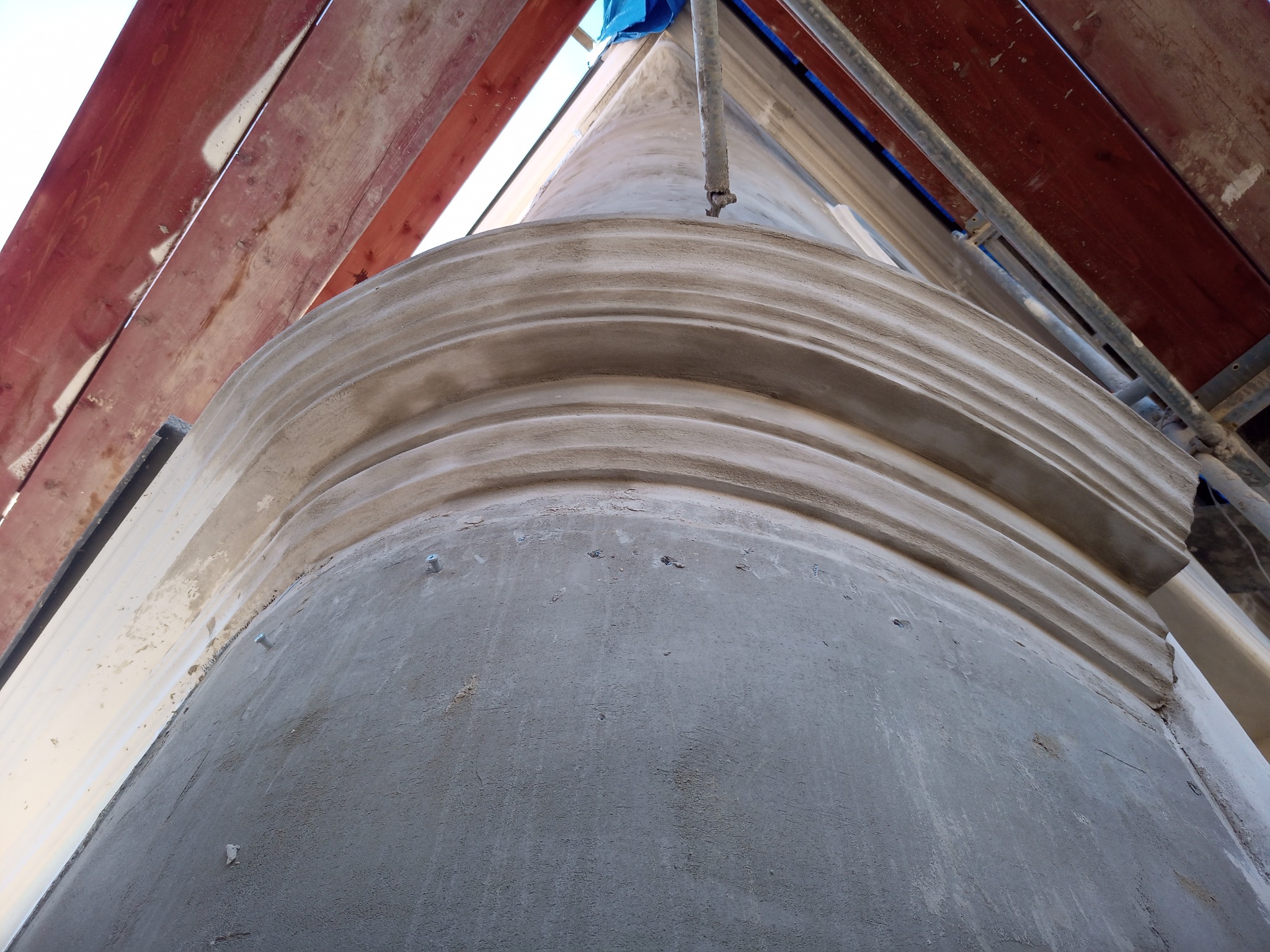 Fragment kolumny z dekoracyjnymi profilami, w trakcie prac renowacyjnych, widoczne ślady po szpachlowaniu i rusztowanie.