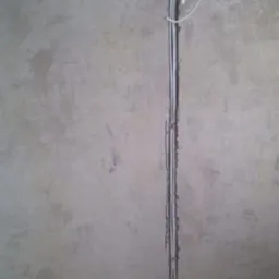 Pionowy montaż przewodów elektrycznych w bruździe na ścianie, z widoczną puszką instalacyjną w Łodzi. Surowy stan ściany przed wykończeniem.