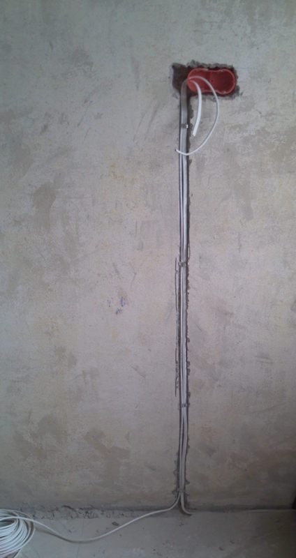 Pionowy montaż przewodów elektrycznych w bruździe na ścianie, z widoczną puszką instalacyjną w Łodzi. Surowy stan ściany przed wykończeniem.